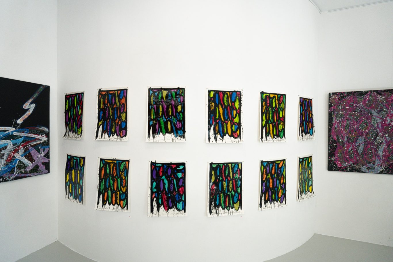 Ensemble de petites œuvres multicolores de JonOne alignées sur deux rangées sur un mur blanc.