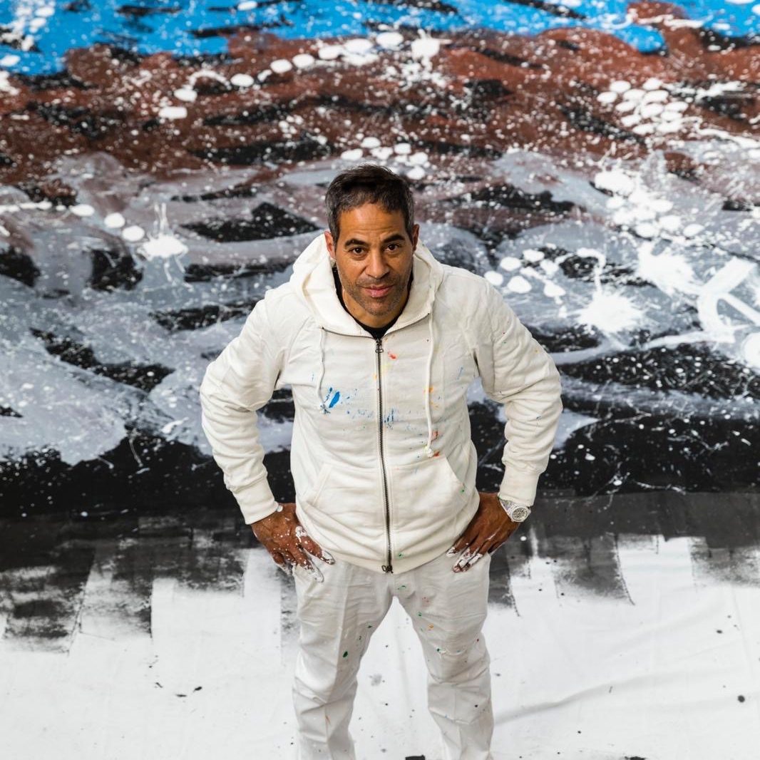 JonOne dans son atelier | H.D Galerie Portrait de JonOne en tenue blanche devant une peinture abstraite noire et blanche.