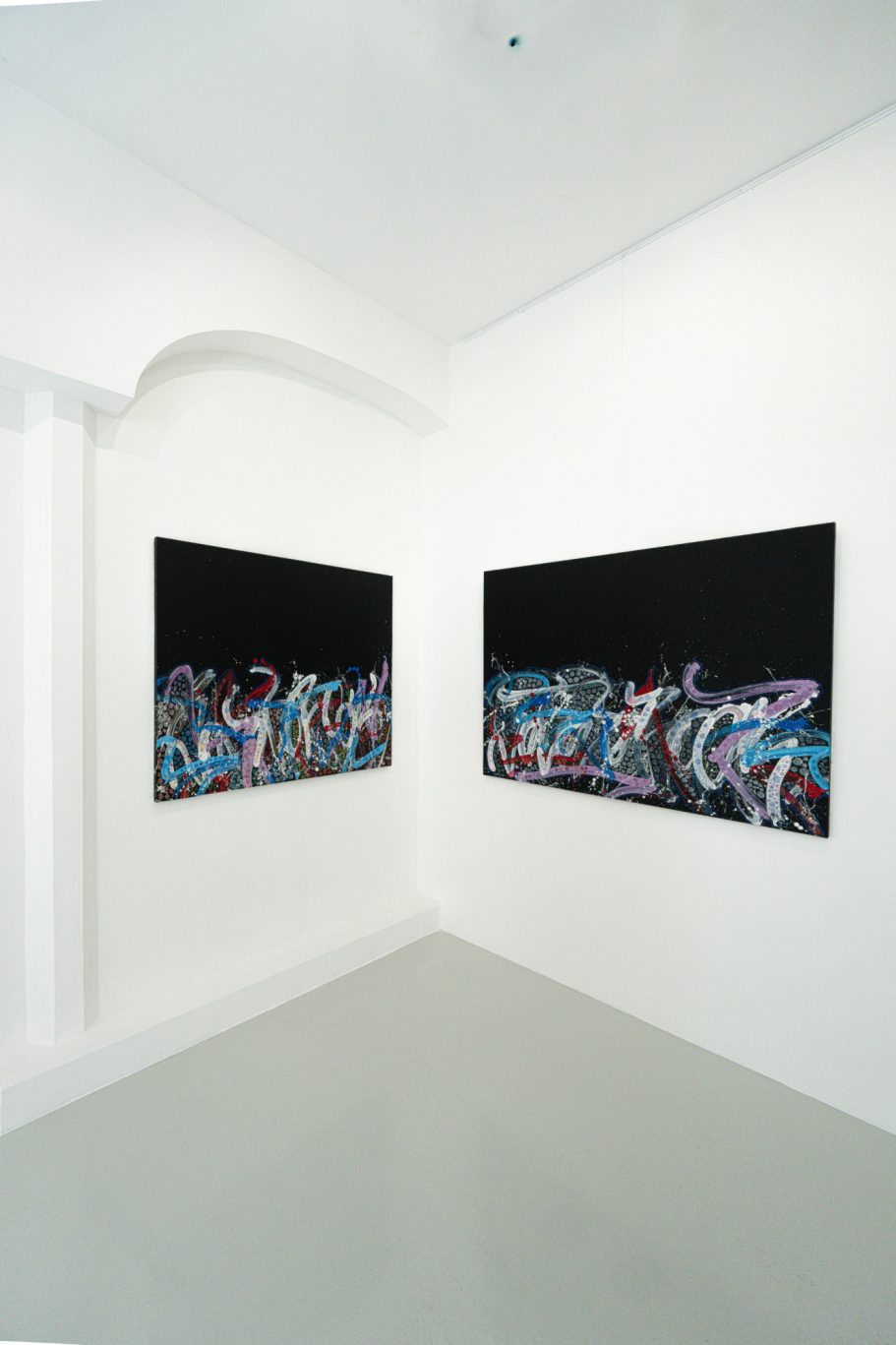 Vue d’un angle de la galerie avec des compositions sur fond noir et des œuvres à dominante bleue.