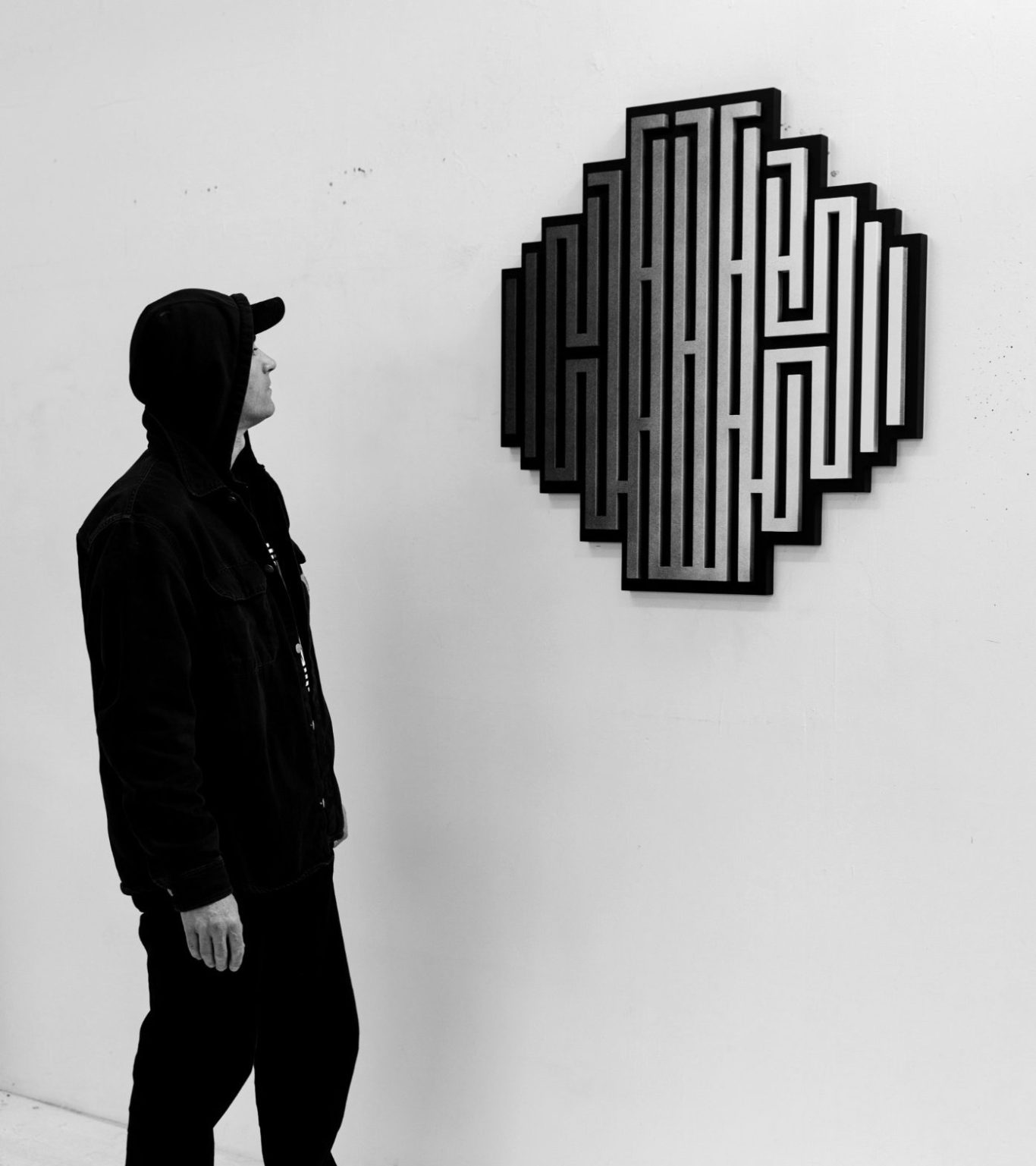 L’artiste L’Atlas observant une œuvre géométrique en noir et blanc lors de l’exposition Révélation chez H.D Galerie à Paris.